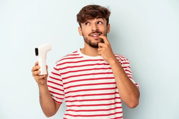 Joven Hombre Raza Mixta Sosteniendo Termómetro Aislado Sobre Fondo Azul —  Fotos de Stock