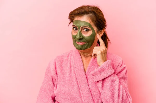 Middle age caucasian woman wearing a facial mask isolated on pink background pointing temple with finger, thinking, focused on a task.