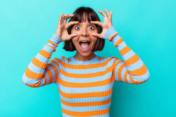 Mavi arka planda izole edilmiş genç melez kadın bir başarı fırsatı bulmak için gözlerini açık tutuyor..