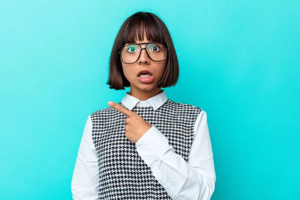 Mavi arka planda izole edilmiş genç bir ırk kadını yan tarafı işaret ediyor.