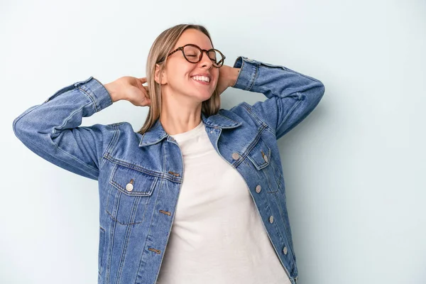 Kafkasyalı genç bir kadın mavi arka planda izole edilmiş, kendinden emin, elleri başının arkasında..