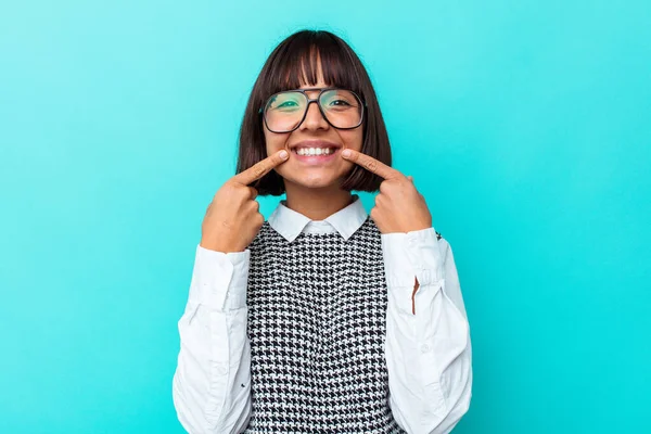 Mavi arka planda izole edilmiş genç bir ırk kadını gülümsüyor, parmaklarını ağzına doğrultuyor..