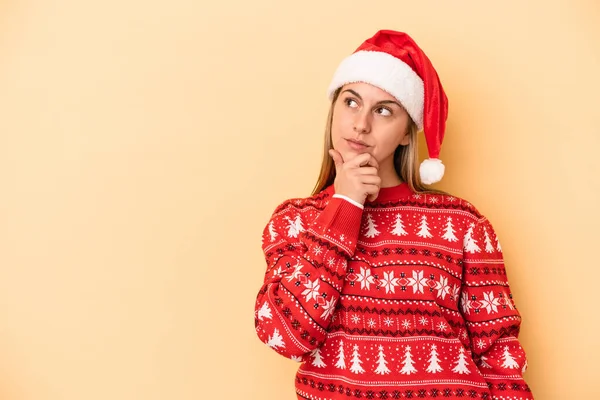 若いですCaucasian女性祝いますクリスマス孤立した上に黄色の背景見て横に疑いと懐疑的な表現 — ストック写真