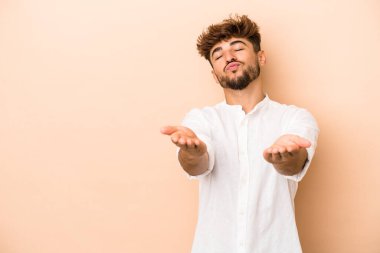 Young arab man isolated on beige background folding lips and holding palms to send air kiss.