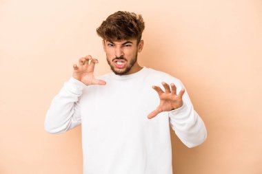 Young arab man isolated on beige background showing claws imitating a cat, aggressive gesture.