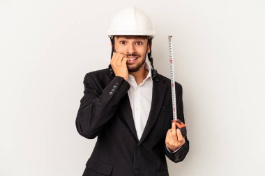 Young mixed race architect man wearing a helmet and holding meter isolated on grey background biting fingernails, nervous and very anxious.