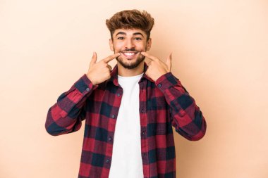 Young arab man isolated on beige background smiles, pointing fingers at mouth.