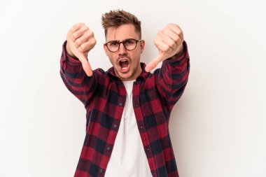 Beyaz arka planda izole edilmiş genç beyaz bir adam baş parmağını aşağı gösteriyor ve hoşlanmadığını ifade ediyor..
