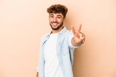 Young arab man isolated on beige background joyful and carefree showing a peace symbol with fingers.