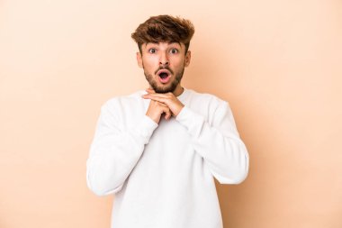 Young arab man isolated on beige background praying for luck, amazed and opening mouth looking to front.