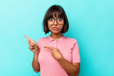 Mavi arka planda izole edilmiş genç melez kadın işaret parmağıyla fotokopi alanını işaret ederek şok oldu..