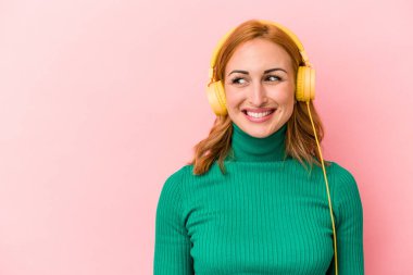 Pembe arka planda izole edilmiş müzik dinleyen beyaz bir kadın.