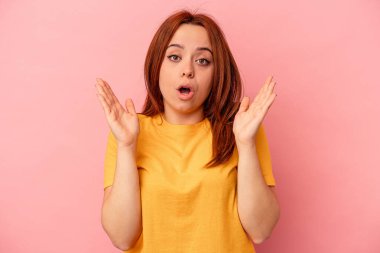 Pembe arka planda izole edilmiş genç beyaz kadın şaşırmış ve şok olmuş..