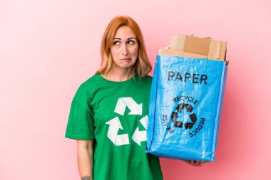 Young caucasian woman recycled paper isolated on pink background confused, feels doubtful and unsure.