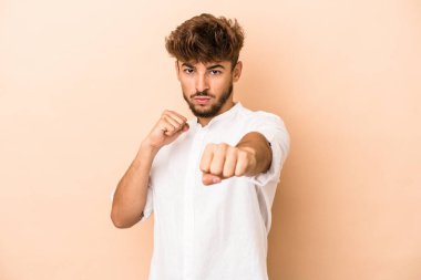 Young arab man isolated on beige background throwing a punch, anger, fighting due to an argument, boxing.