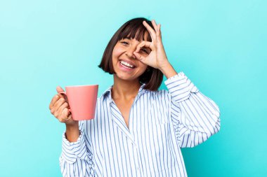 Mavi arka planda pembe kupa tutan genç bir ırk kadını heyecanlı..