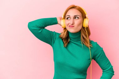Pembe arka planda izole edilmiş müzik dinleyen beyaz bir kadın kafasının arkasına dokunuyor, düşünüyor ve bir seçim yapıyor..