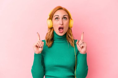 Pembe arka planda izole edilmiş müzik dinleyen beyaz bir kadın ağzı açık bir şekilde üst tarafı işaret ediyor..