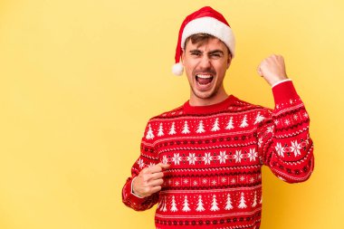 Sarı arka planda izole edilmiş genç beyaz adam zaferden sonra yumruğunu kaldırıyor, kazanan konsept..