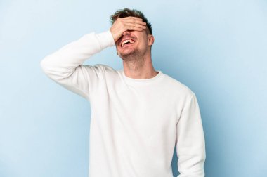 Mavi arka planda izole edilmiş genç beyaz adam ellerini başının üstünde tutarak neşe içinde gülüyor. Mutluluk kavramı.