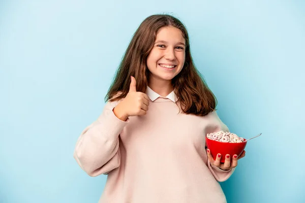 小高加索女孩拿着一碗谷物 蓝色背景隔离 微笑着举起大拇指 — 图库照片
