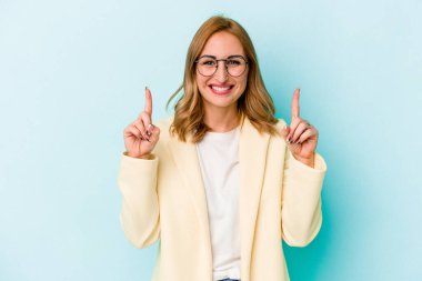 Mavi arka planda izole edilmiş genç beyaz kadın iki parmağı da boş bir alan gösteriyor..