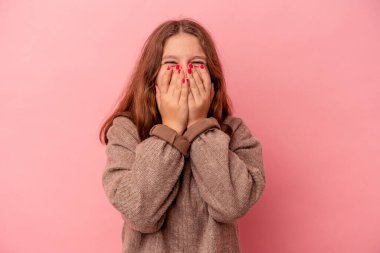 Pembe arka planda izole edilmiş küçük beyaz kız bir şeye gülüyor, elleriyle ağzını kapatıyor..