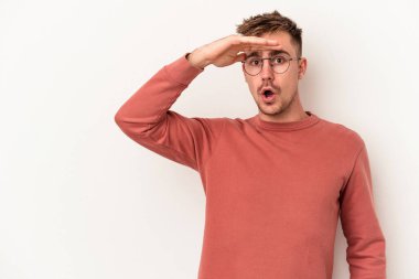 Beyaz arka planda izole edilmiş genç beyaz bir adam uzaklara bakıyor ve elini alnına koyuyor..