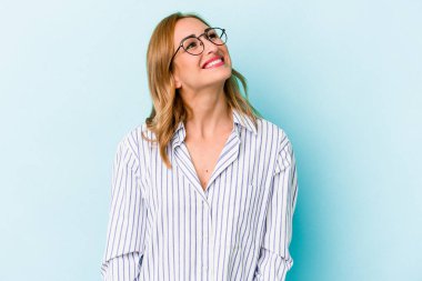 Genç beyaz kadın mavi arka planda izole edilmiş rahat ve mutlu bir şekilde gülüyor, boynunda dişlerini gösteriyor..