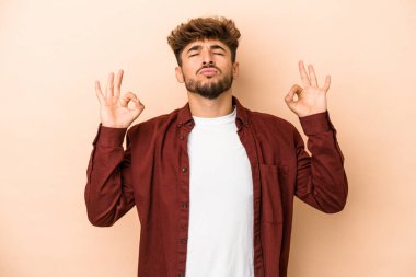 Young arab man isolated on beige background relaxes after hard working day, she is performing yoga.