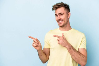 Kafkasyalı genç adam mavi arka planda izole edilmiş. İşaret parmağıyla işaret ettiği için heyecanlı..