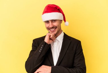 Yeni yılı kutlayan beyaz bir genç adam sarı arka planda izole edilmiş bir Noel şapkası takıyor.