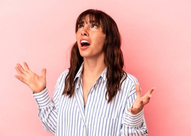 Arjantinli genç bir kadın pembe arka planda izole edilmiş, gökyüzüne haykırıyor, yukarı bakıyor, hayal kırıklığına uğramış.