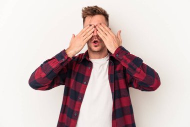 Beyaz arka planda izole edilmiş genç beyaz bir adam elleriyle gözlerini kapatmaktan korkuyor..