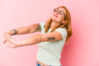 Pembe arka planda izole edilmiş genç beyaz kadın kollarını uzatıyor, rahat bir konumda..