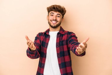 Young arab man isolated on beige background showing a welcome expression.