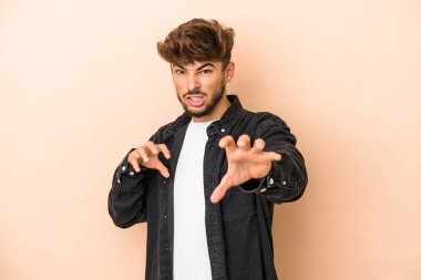 Young arab man isolated on beige background showing claws imitating a cat, aggressive gesture.