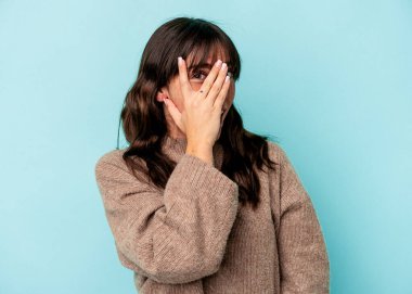 Arjantinli genç bir kadın mavi arka planda izole edilmiş. Kameraya parmaklarıyla göz kırpıyor. Yüzünü kapatmaktan utanıyor..