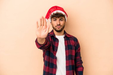 Young arab man celebrating Christmas isolated on beige background standing with outstretched hand showing stop sign, preventing you.