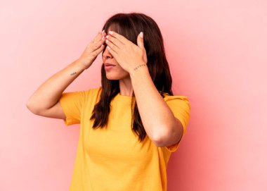 Arjantinli genç bir kadın pembe arka planda izole edilmiş, elleriyle gözlerini kapatmaktan korkuyor..