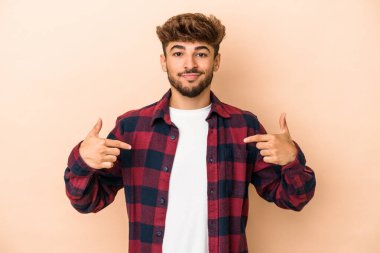 Young arab man isolated on beige background person pointing by hand to a shirt copy space, proud and confident