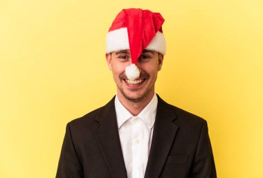 Yeni yılı kutlayan beyaz bir genç adam sarı arka planda izole edilmiş bir Noel şapkası takıyor.