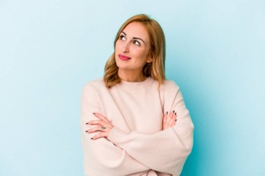 Mavi arka planda izole edilmiş genç beyaz kadın hedeflerine ve amaçlarına ulaşma hayali kuruyor.