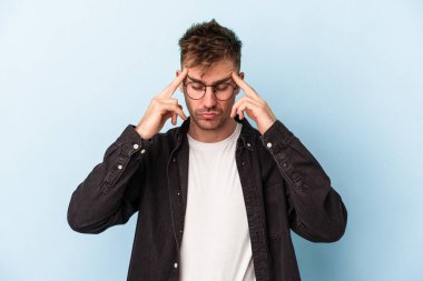 Kafkasyalı genç bir adam mavi arka planda izole edilmiş, başı ağrıyor, yüzüne dokunuyor..