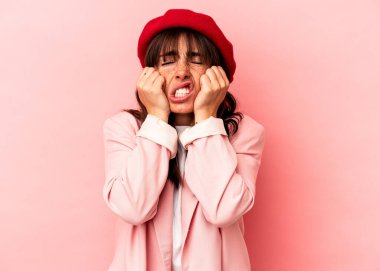 Arjantinli genç bir kadın pembe arka planda izole edilmiş, ağlıyor, bir şeyden memnun değil, acı ve kafa karışıklığı konsepti..