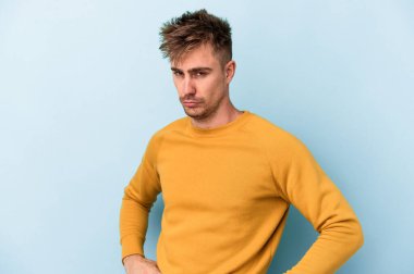 Kafkasyalı genç adam mavi arka planda izole edilmiş hoşnutsuzca kaşlarını çatmış, kollarını kavuşturmuş..