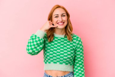 Pembe arka planda izole edilmiş genç beyaz kadın parmaklarıyla bir cep telefonu hareketi gösteriyor..