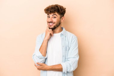 Young arab man isolated on beige background smiling happy and confident, touching chin with hand.