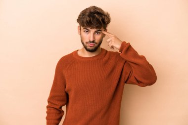 Young arab man isolated on beige background pointing temple with finger, thinking, focused on a task.