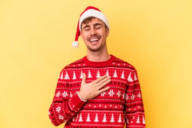 Sarı arka planda izole edilmiş bir şekilde Noel 'i kutlayan Kafkasyalı genç adam elini göğsünde tutarak kahkahalar atıyor..